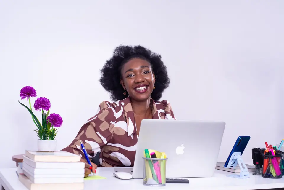 A smiling business owner working at her desk, phone beside her laptop
